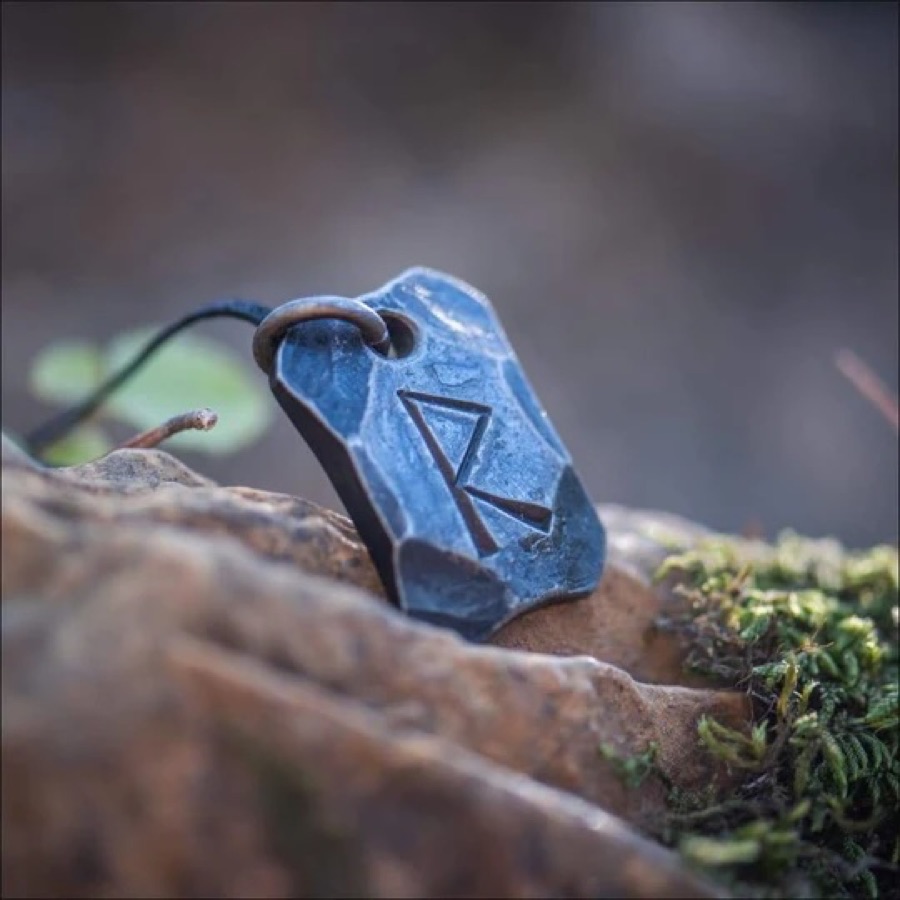 A hand-forged iron pendant carved with the Raidho rune, resting on stone and moss
